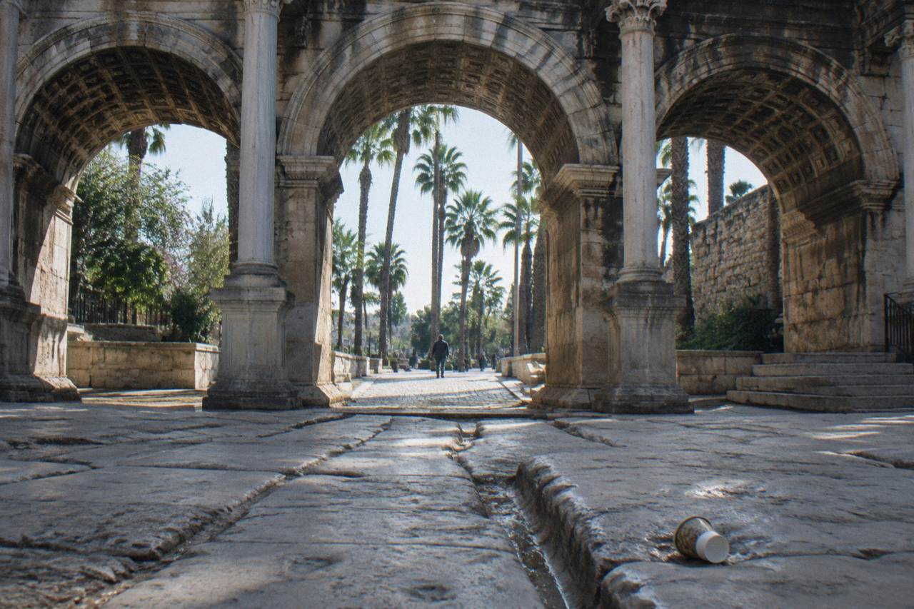 A stone gate with tall arches opening onto a cobbled old town street in Antalya