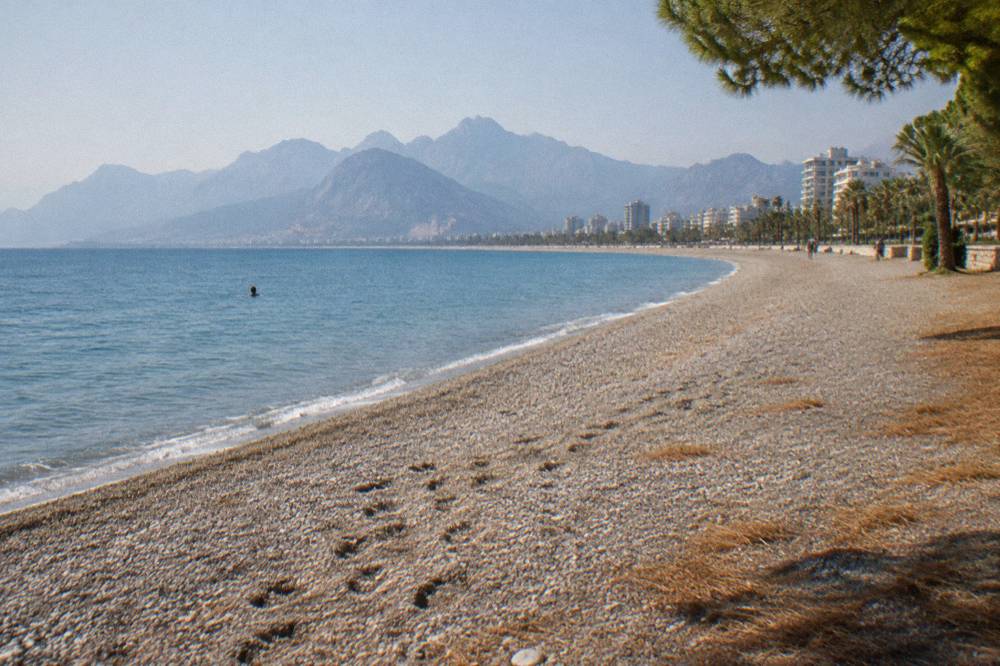 An open pebble beach with people-free sand and calm sea along a wide bay