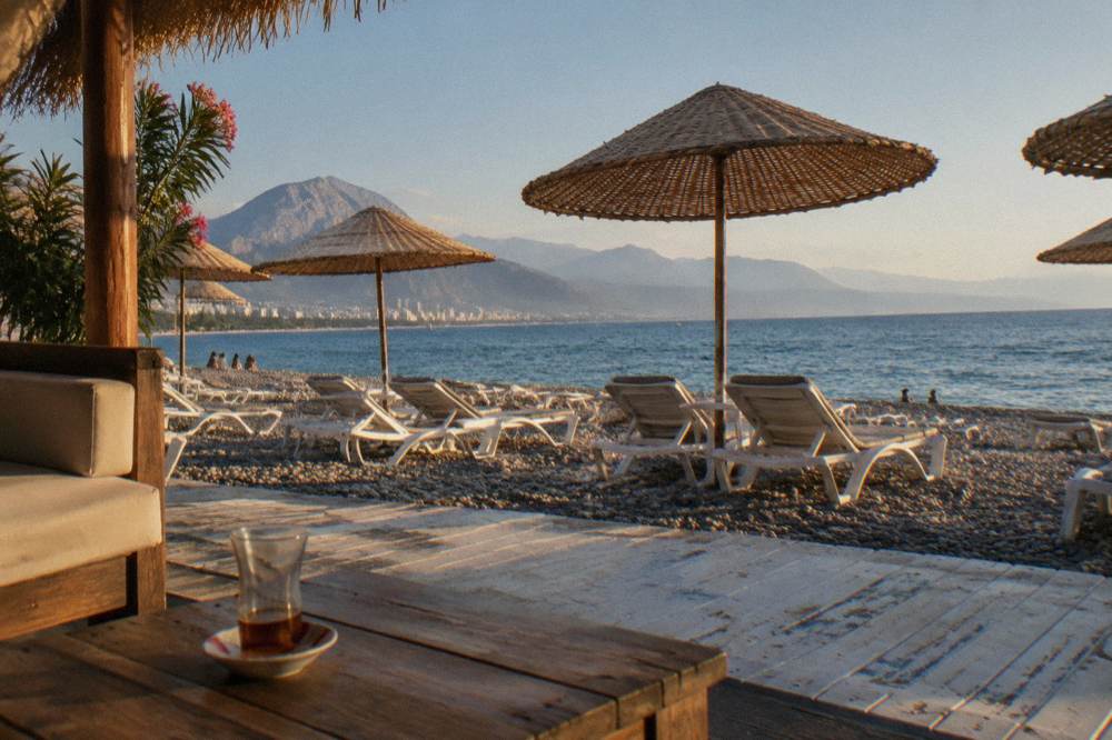 A beach club area with empty sunbeds under straw umbrellas facing the sea