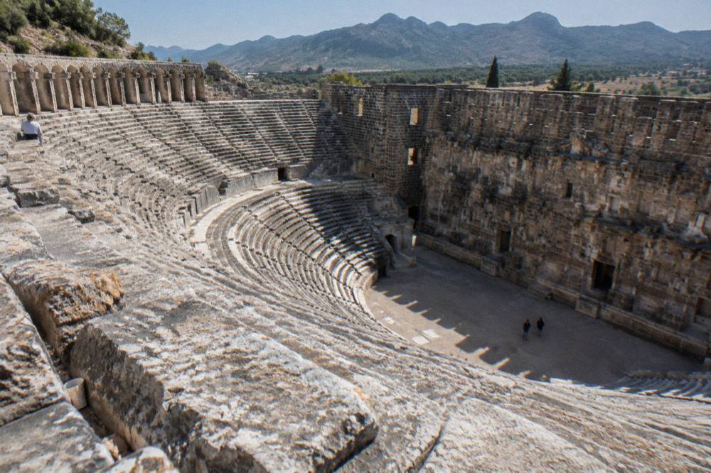 Rows of stone seating curving around the Aspendos theatre bowl in late afternoon light