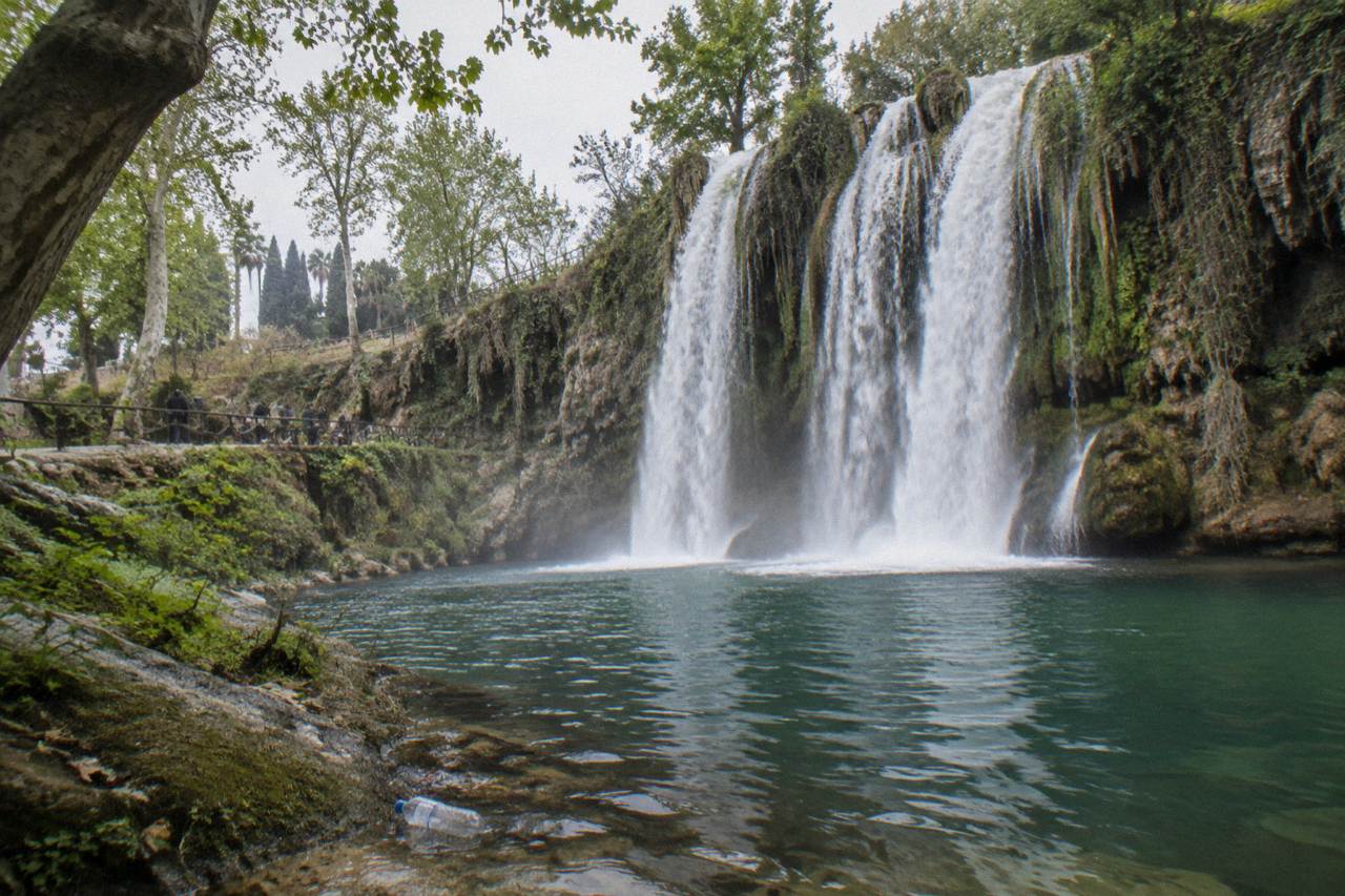 A wide waterfall dropping over a rocky cliff into a pool surrounded by trees