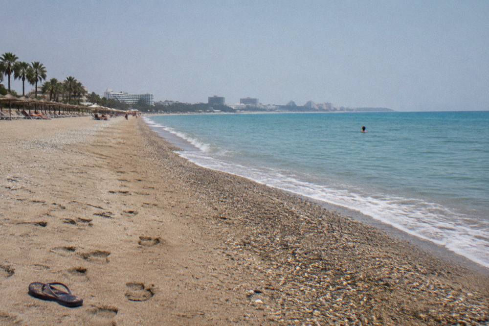 A long Antalya beach with a sand and pebble shore beside calm water