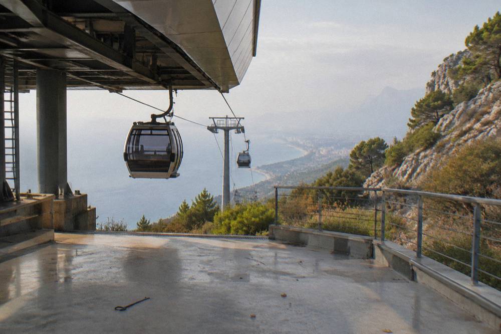A stationary cable car station platform with empty cabins and a coastal hill beyond