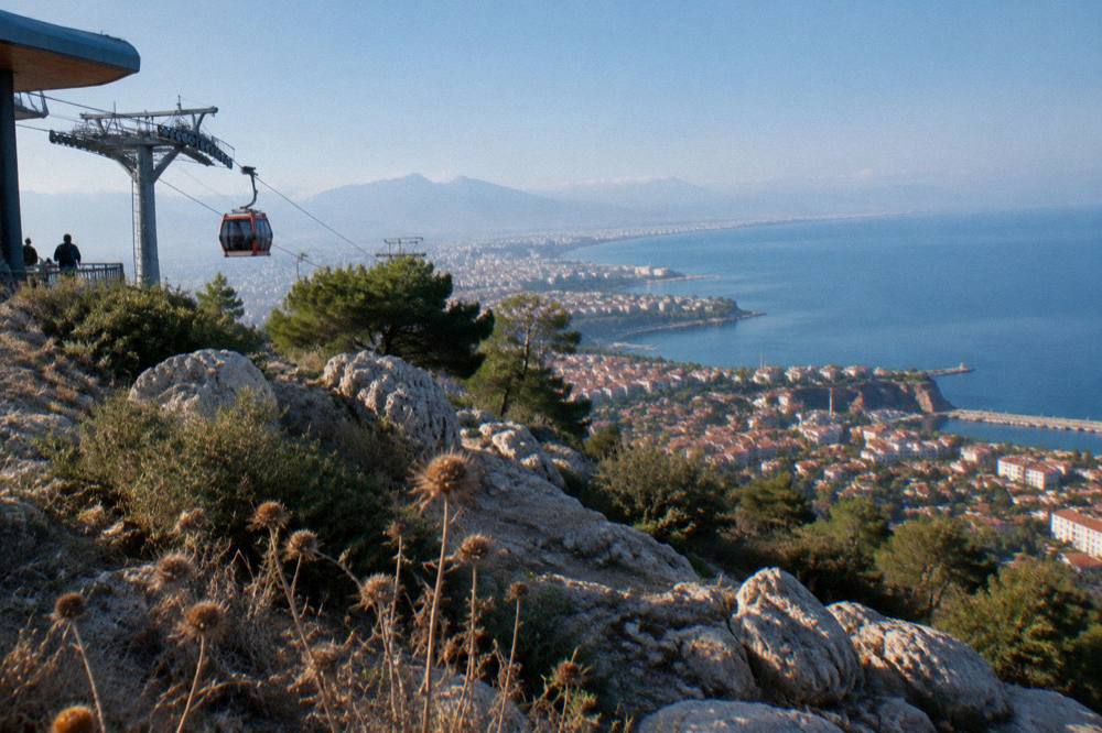 A coastal hilltop with a calm sea and distant city rooftops under a clear sky