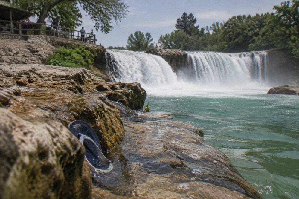 A wide waterfall flowing over a rocky ledge into a pool surrounded by trees