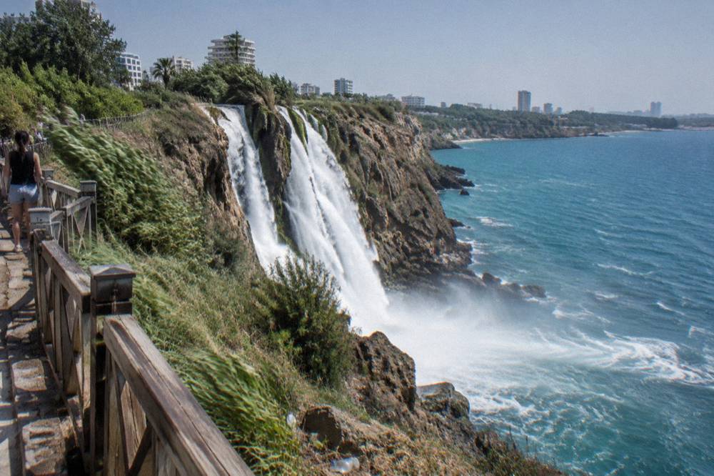 Water falling from a cliff directly into the sea seen from a park viewing area