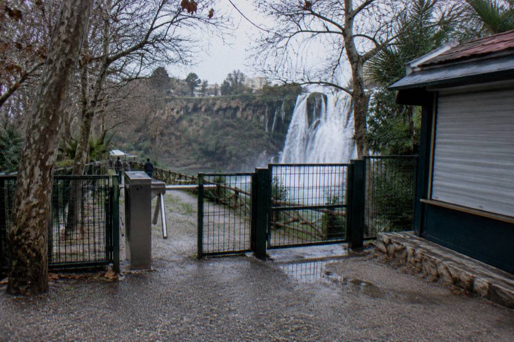 A fenced park entrance with a waterfall beyond the trees
