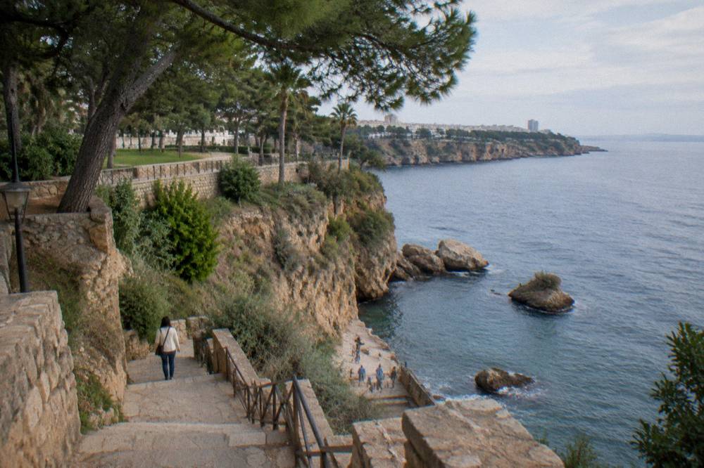 A small cove beach at the base of cliffs with a stone stairway leading down