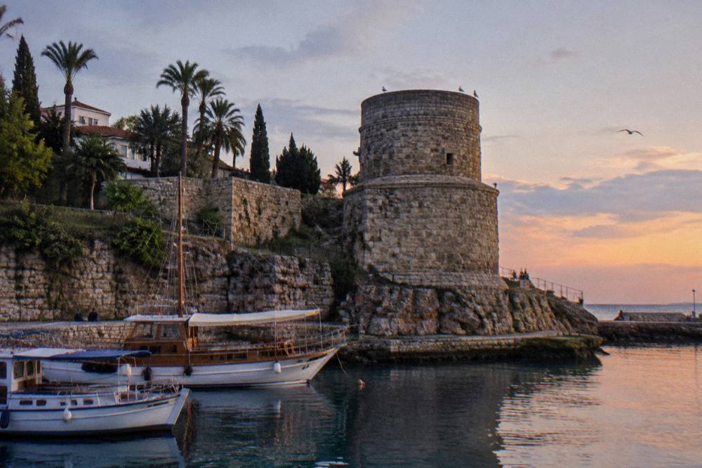 Stone harbour walls with moored boats and a stone tower above the water