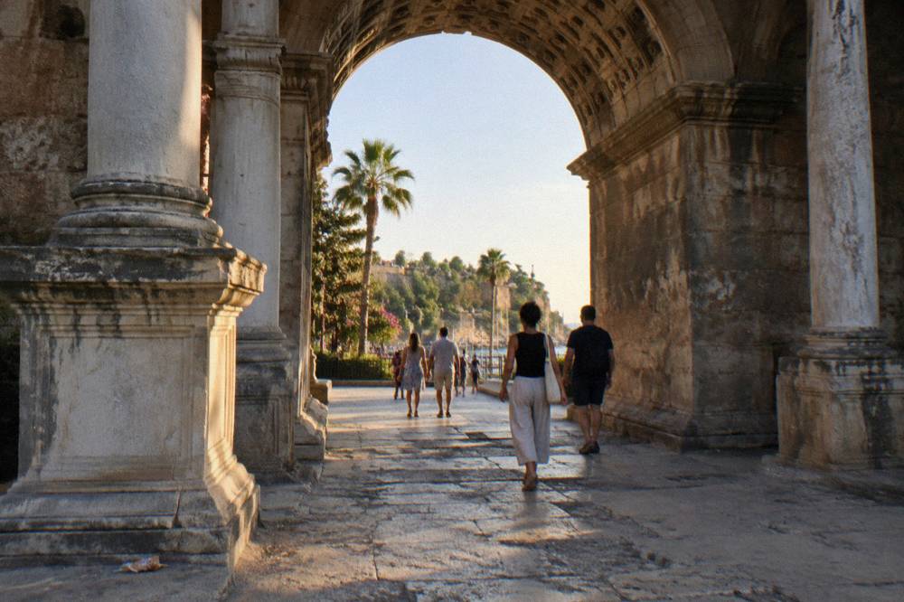 People passing on foot through the open arch of a stone gate in Antalya