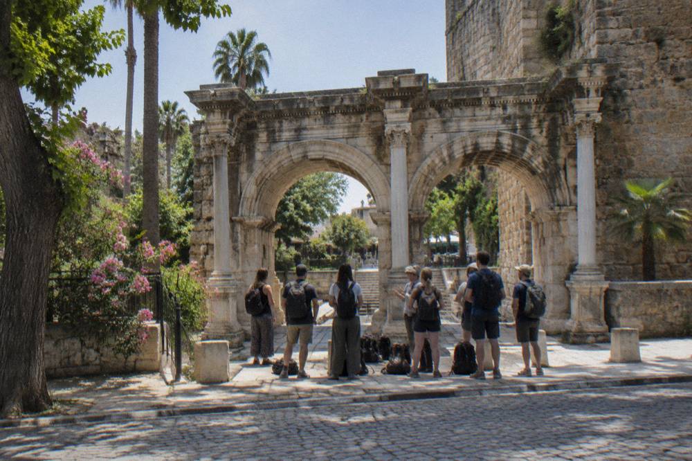 A guided group of walkers gathered at a stone gate in Antalya old town
