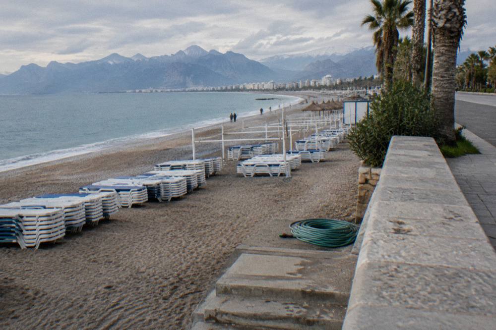 A wide city beach with rows of empty sunbeds and a stone promenade behind the sand