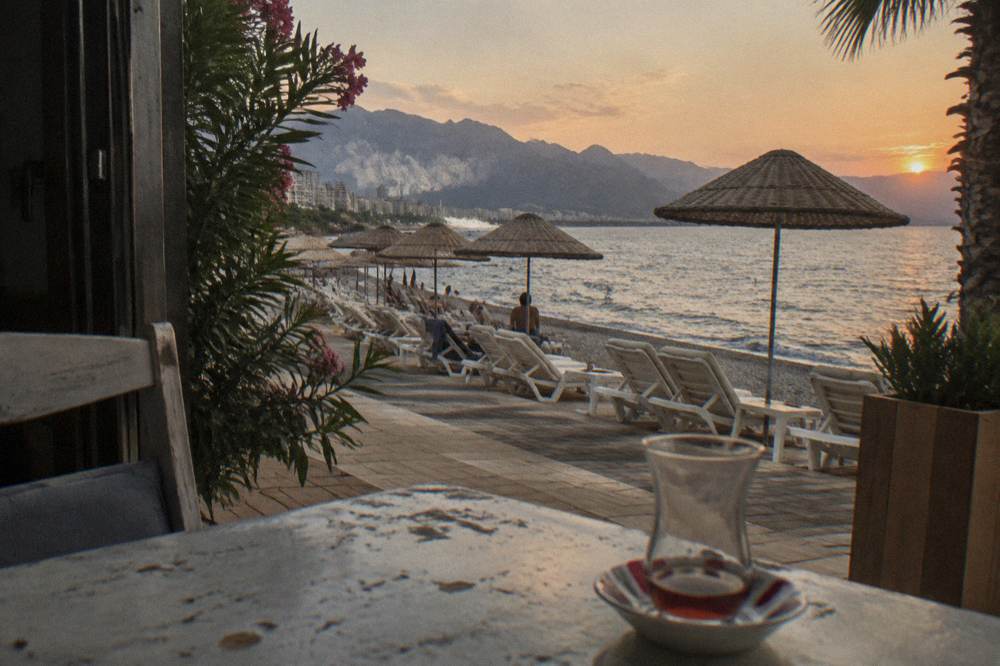 Rows of white sunbeds and straw umbrellas on a beach club terrace above the water