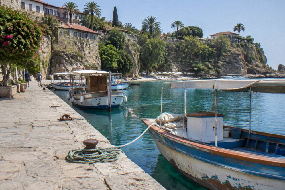 A stone harbour wall with wooden boats moored along a calm waterfront at midday