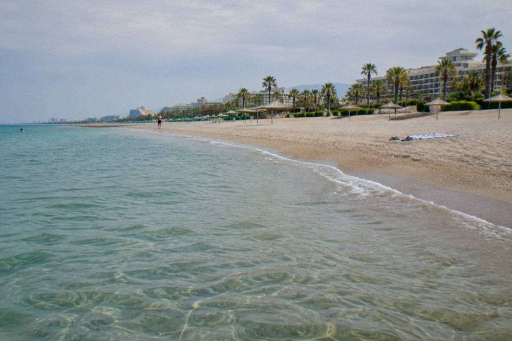 Curving sandy shoreline with clear water and parasols spaced along the sand