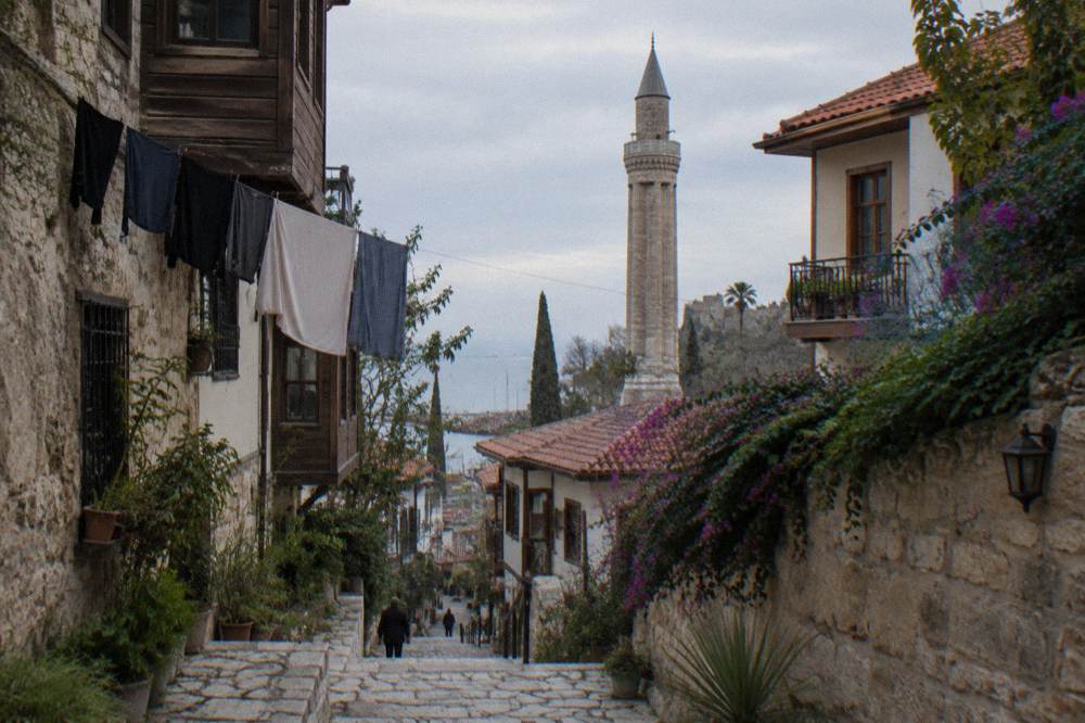 A narrow old town street with stone walls and a stone tower rising above the rooftops